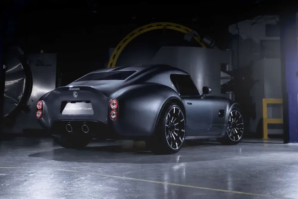 Voiture électrique AC Cobra GT Coupé noire, design rétro, stationnée dans un garage sombre.