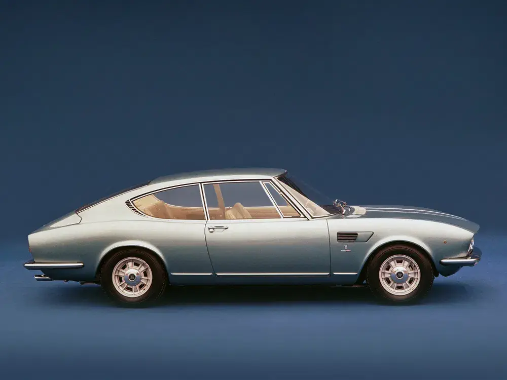 Voiture classique Fiat Dino 2400 bleu clair, design élégant, fond bleu.