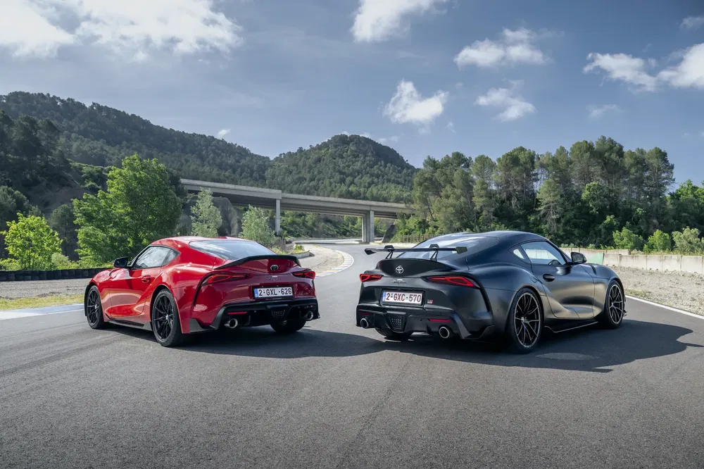 Twee Toyota Supra's 2023, rood en zwart, op een schilderachtige bergweg.