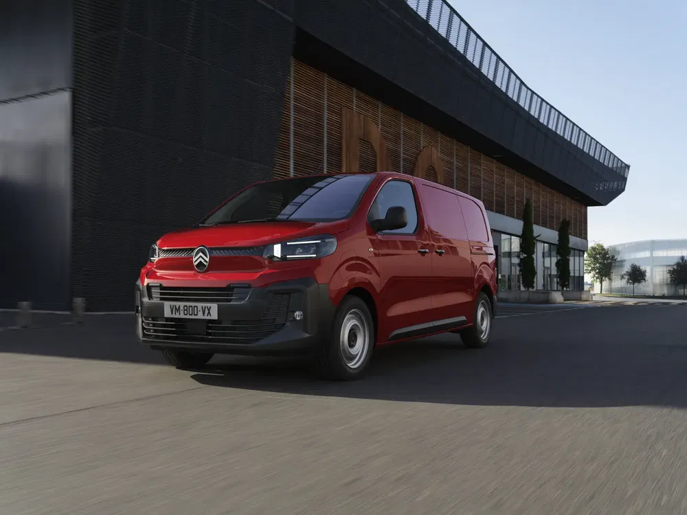 Fourgon Citroën rouge roulant près d'un bâtiment moderne, idéal pour une utilisation urbaine.
