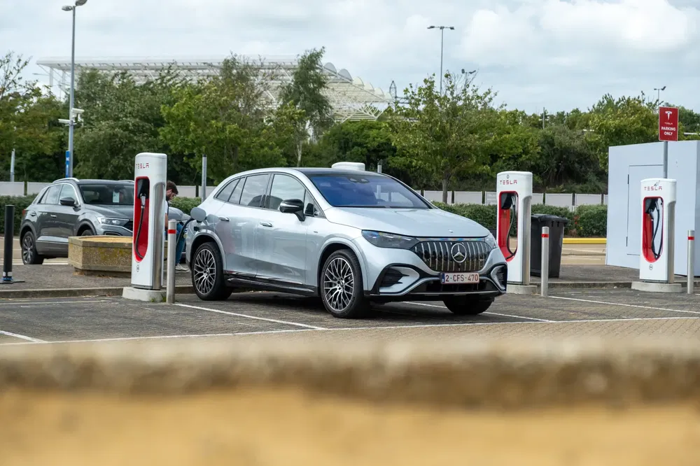 Mercedes EQS recharge sur une borne Tesla en plein air, stationnement ombragé.