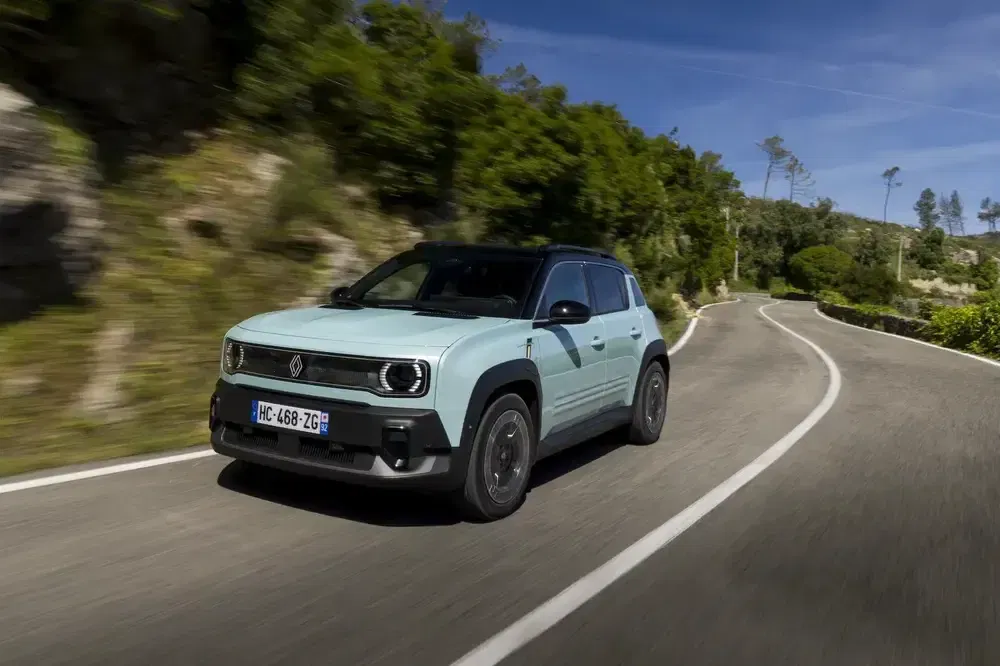 Renault 4 moderne roulant sur une route sinueuse bordée de verdure.