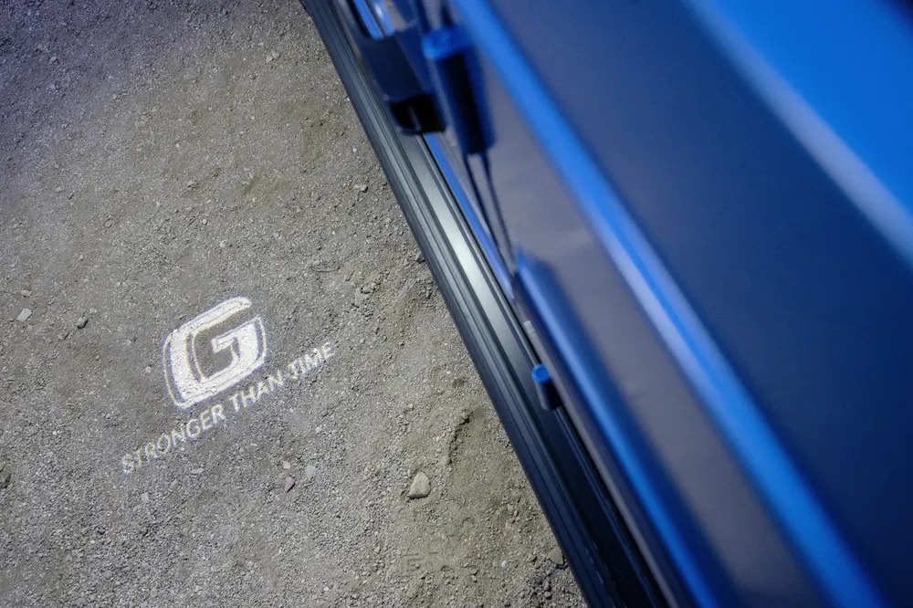 Logo G avec slogan 'Stronger Than Time' projeté sur le sol à côté d'un véhicule.