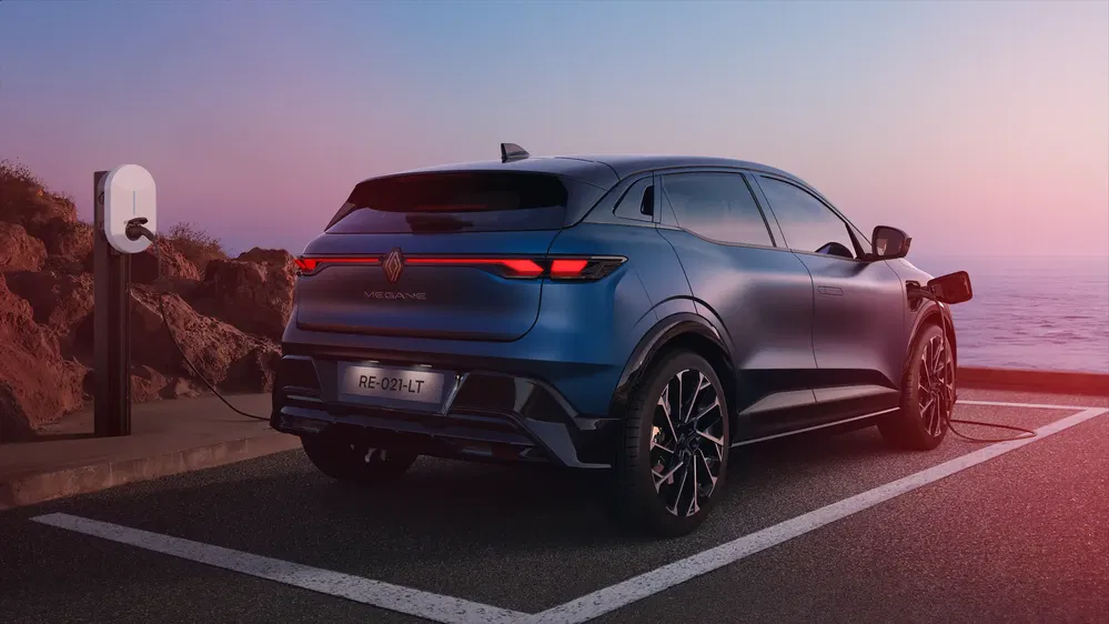 Elektrische Renault Mégane laadt op aan zee bij schemering, achterlichten verlicht.