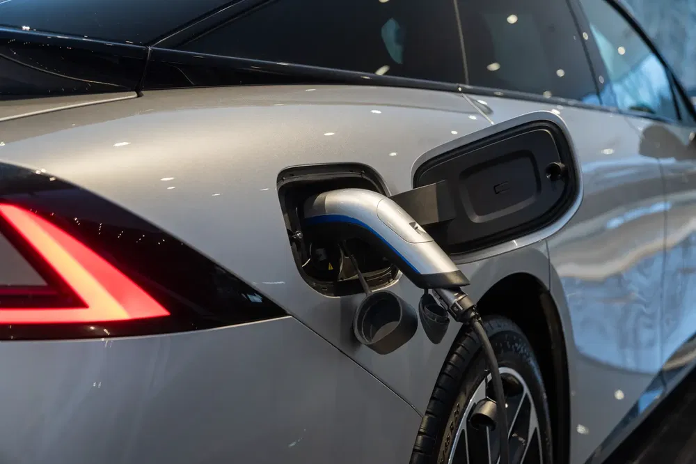 Zilveren elektrische auto laadt op met een kabel aangesloten op de achterste poort.