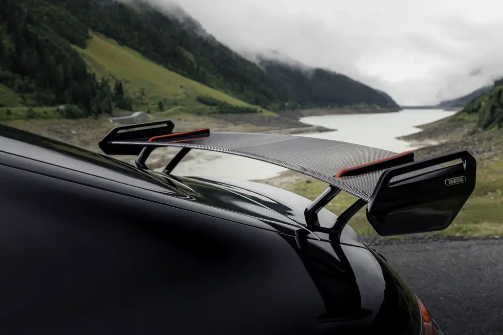 Aileron arrière en fibre de carbone d'une voiture de sport au bord d'un lac alpin.
