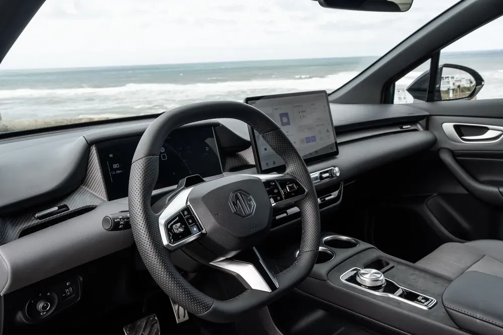 Moderne MG-auto-interieur, stuurwiel en schermen met uitzicht op zee.