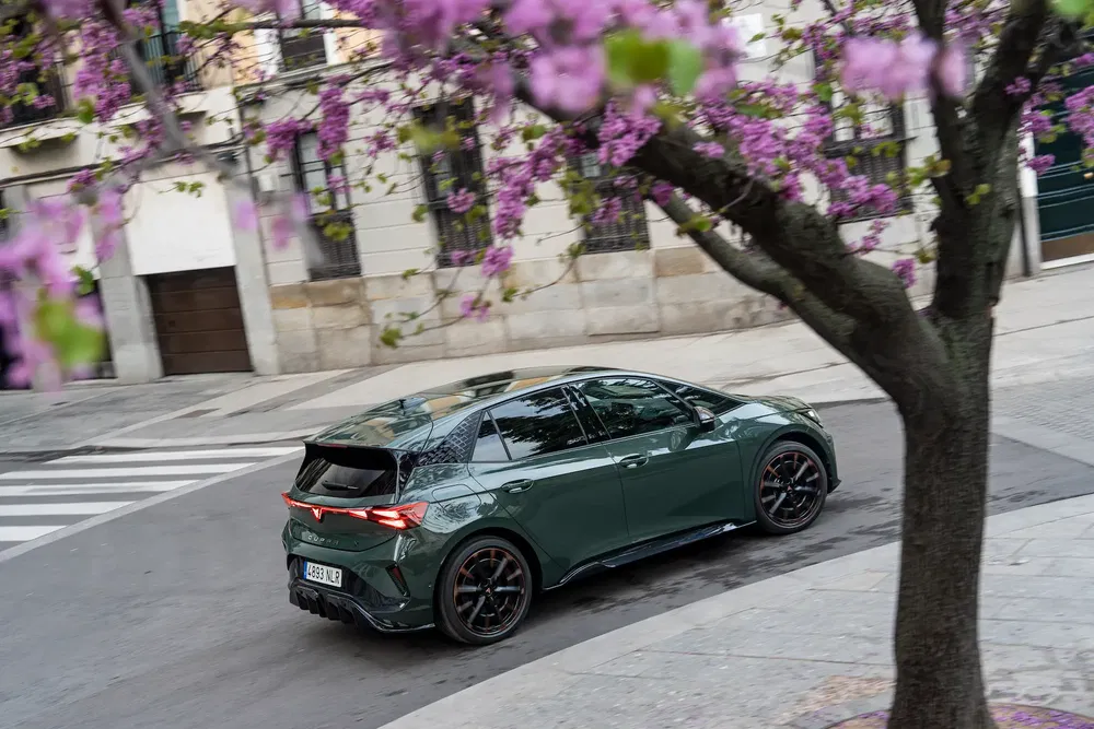 Cupra Born électrique passant sous des arbres en fleurs dans une rue de la ville.
