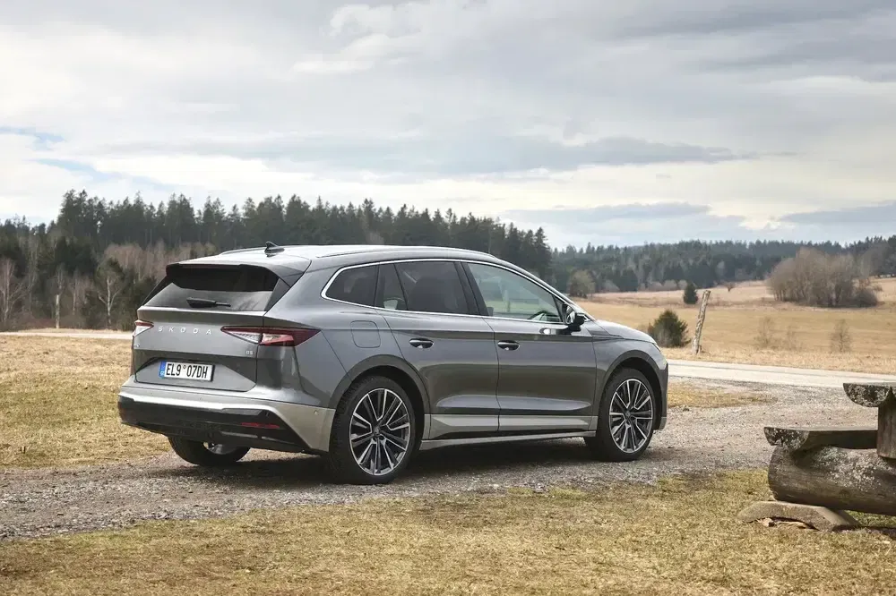 Zilveren Skoda Enyaq geparkeerd in landelijke omgeving onder bewolkte hemel.