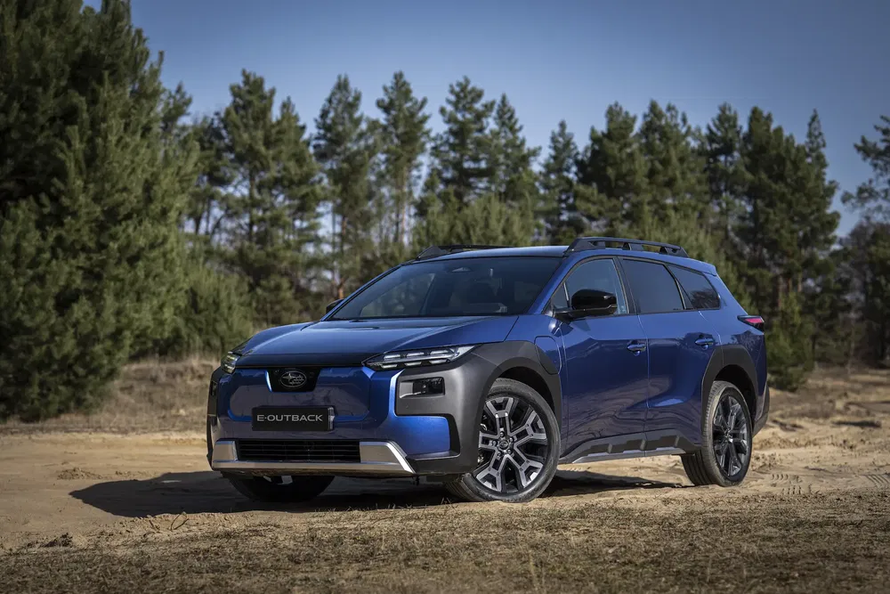 Subaru Outback e-Boxer bleu garé en plein air devant une rangée d'arbres verts.