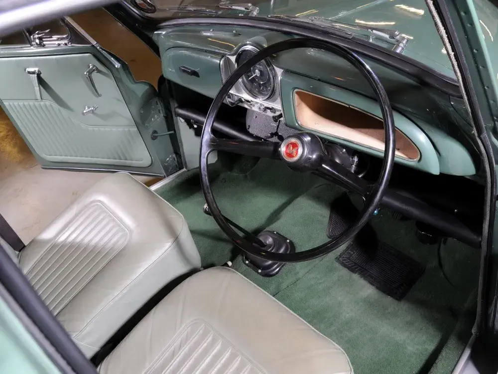 Intérieur vintage d'une voiture Morris Minor avec sièges en cuir vert et tableau de bord classique.