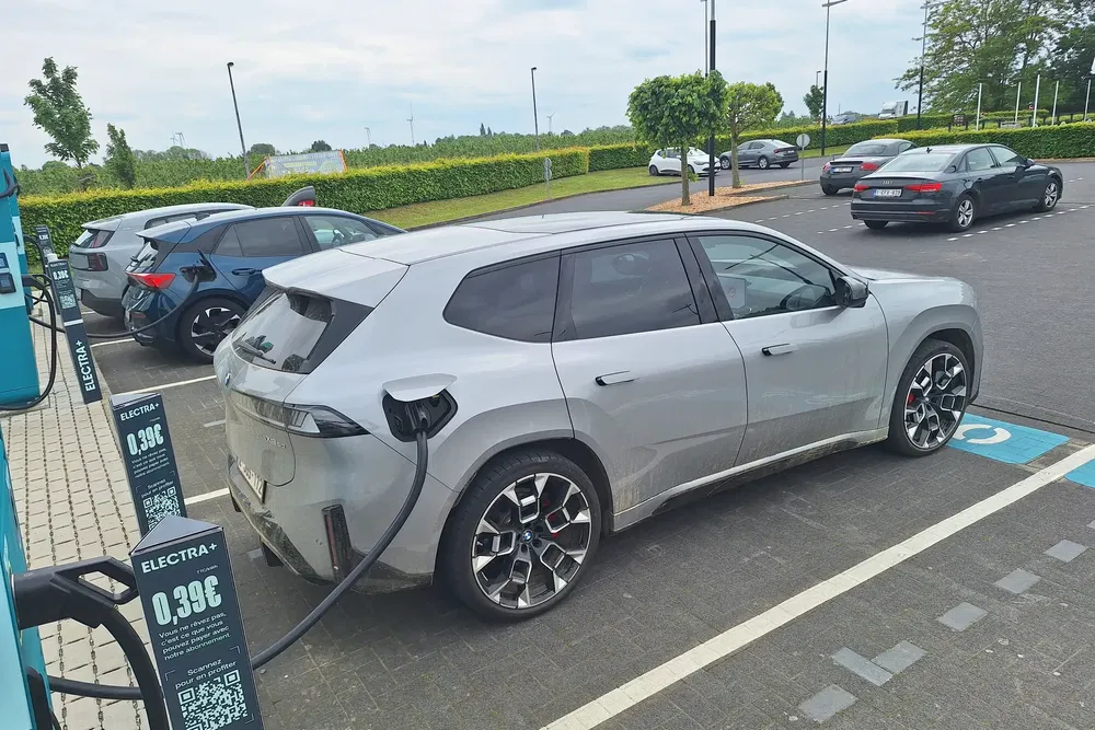 BMW électrique iX en charge à une station Electra, parking arboré en arrière-plan.