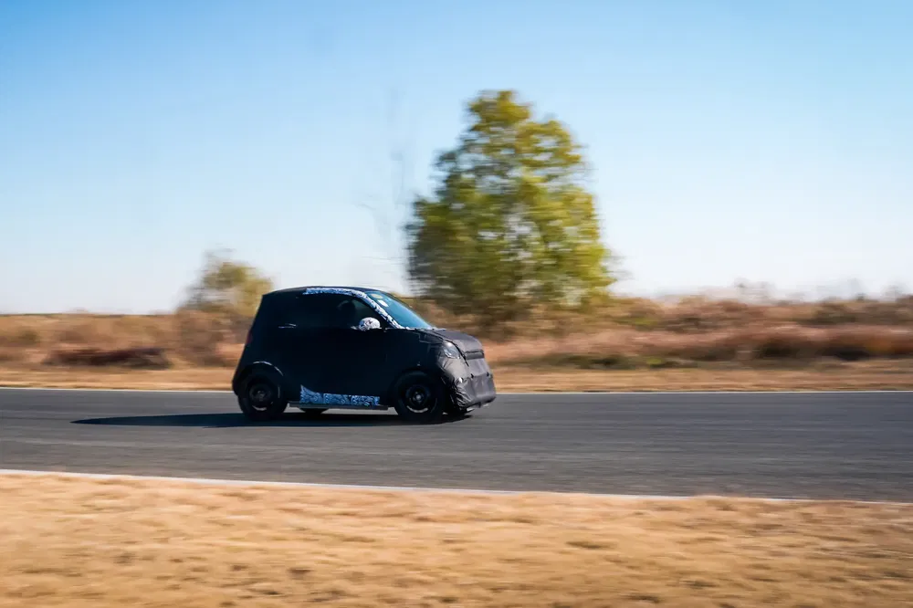 Prototype de voiture noire camouflée, testant la vitesse sur une piste de course en plein air.