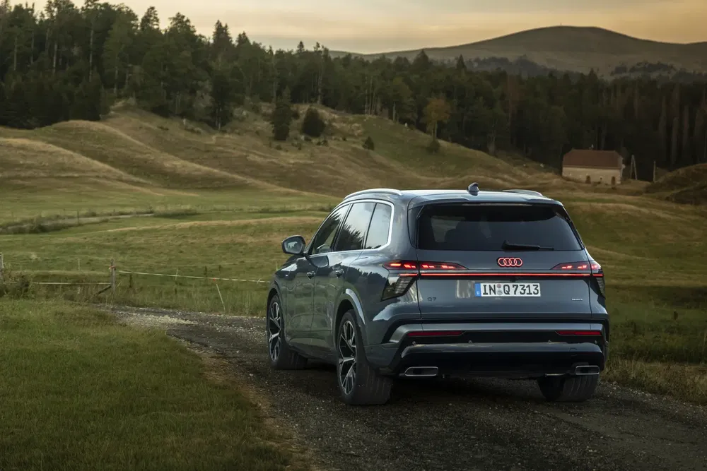 Audi Q7 sur chemin de campagne avec paysage vallonné et horizon boisé.