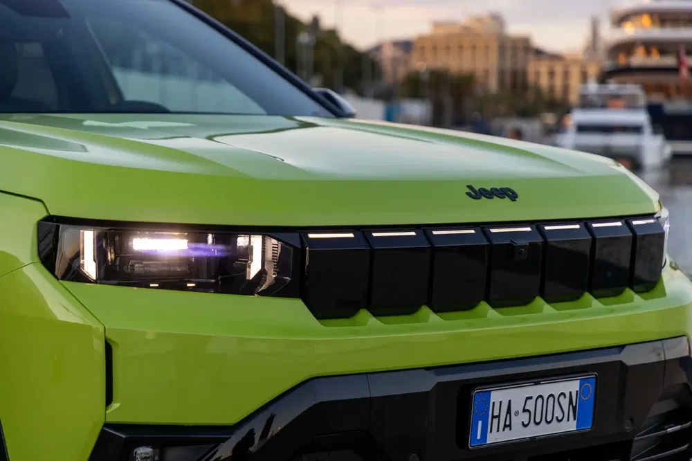 Voorgrille van een groene Jeep met brandende koplamp en Italiaanse kentekenplaat.