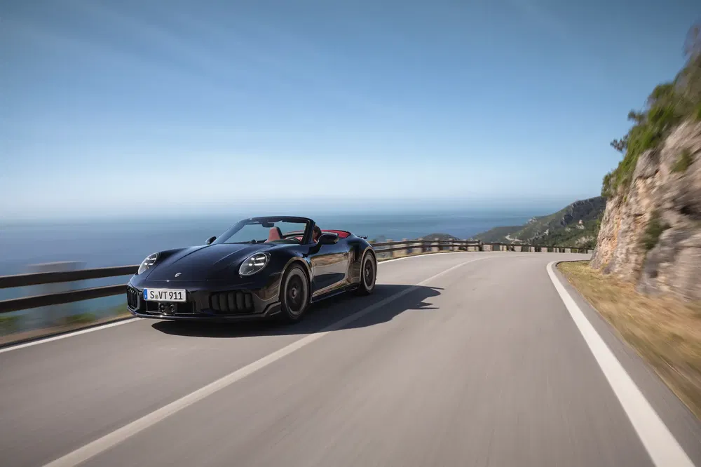 Porsche 911 Cabriolet noir roulant sur une route côtière sinueuse et panoramique.