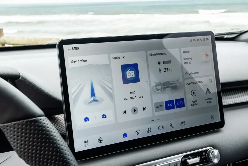 Auto-infotainment-touchscreen met navigatie, radio en klimaatregeling aan zee.