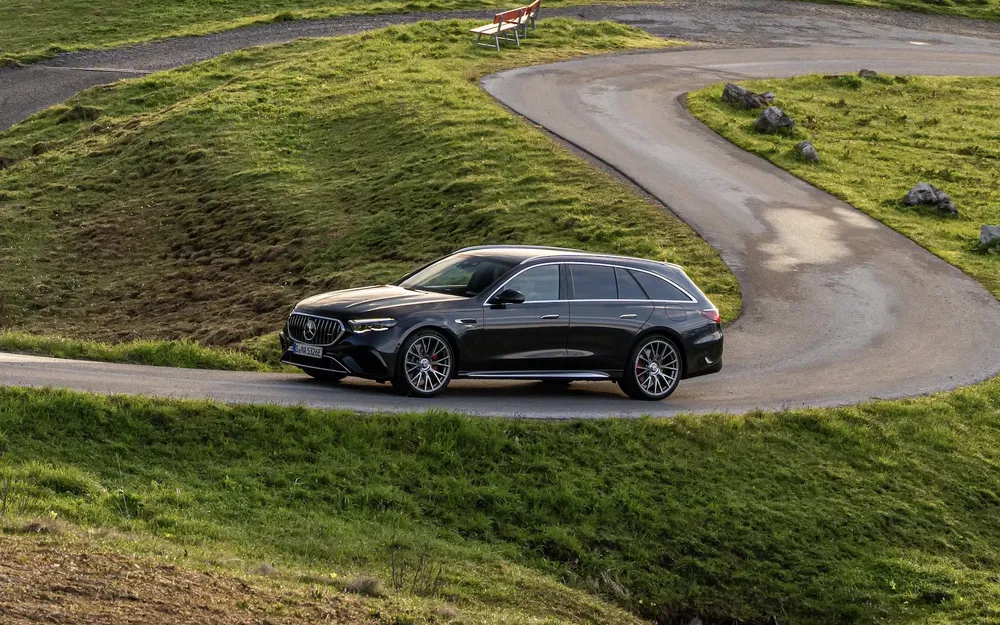 Mercedes Classe E break roulant sur une route sinueuse entourée de collines verdoyantes.