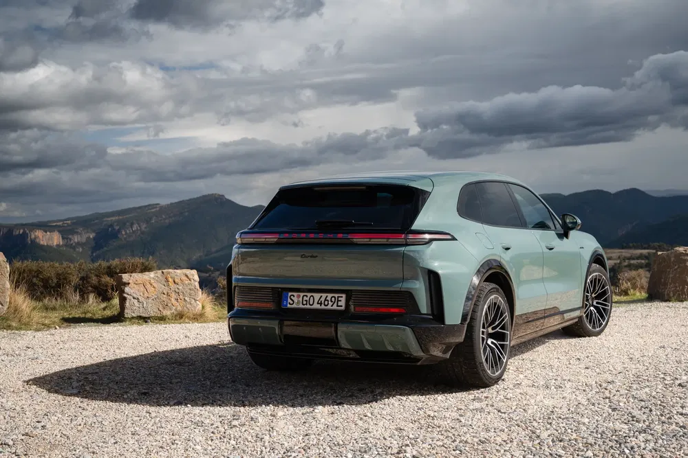 Porsche Cayenne vert stationné avec vue sur montagne nuageuse en arrière-plan.