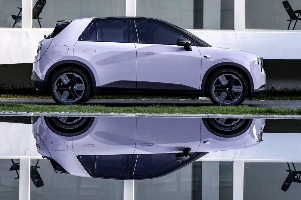 Voiture électrique compacte, C-Crossover blanc avec reflet sur l'eau devant un bâtiment moderne.