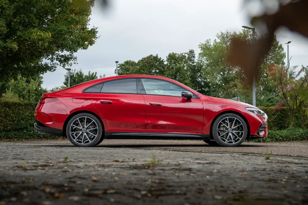 Rode Mercedes-Benz CLA zijaanzicht, geparkeerd op een met bomen omzoomde weg.