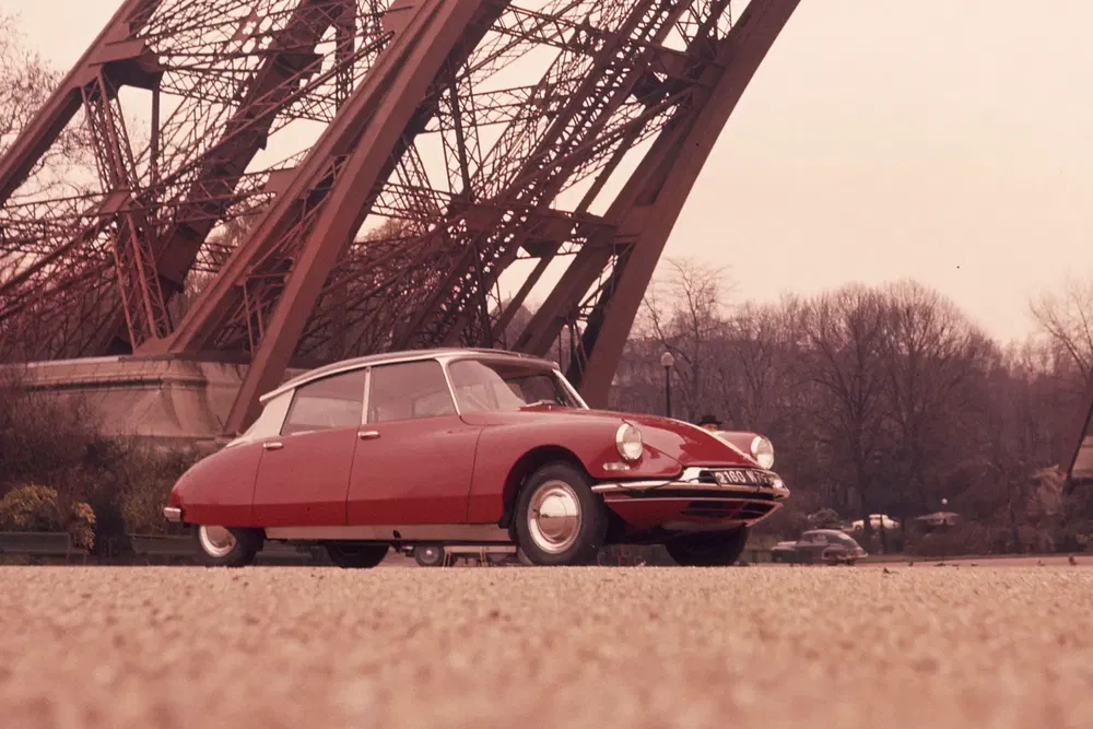 Citroën DS rouge stationnée sous la Tour Eiffel, ambiance vintage et élégance française.