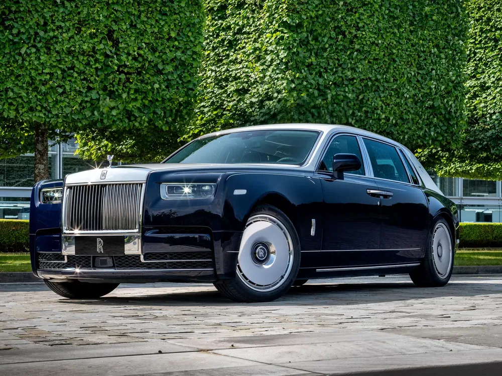 Rolls-Royce Phantom noire luxueuse stationnée devant des arbres taillés impeccablement.
