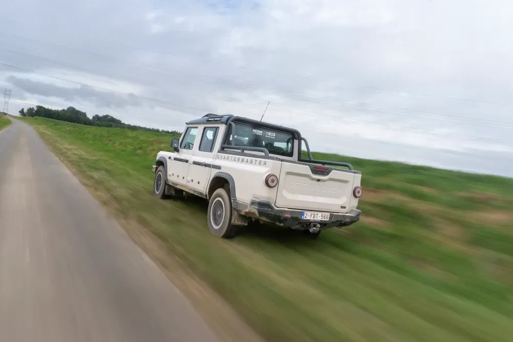 Ineos Grenadier pick-up rijdt op landelijke weg met bewolkte lucht.