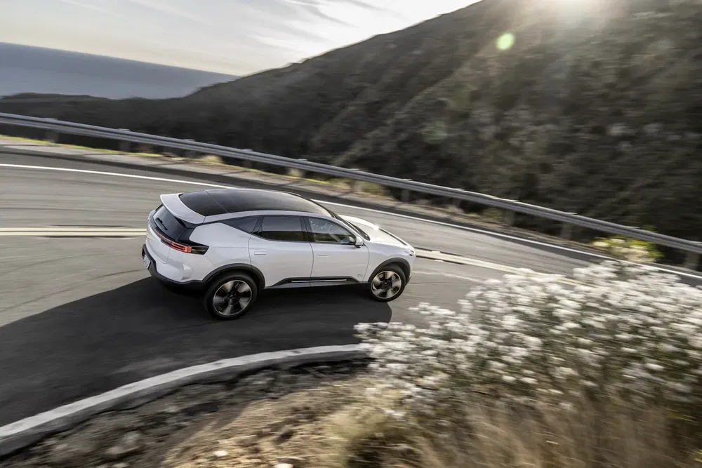 Toyota bZ4X blanc prenant un virage sur une route de montagne en journée ensoleillée.