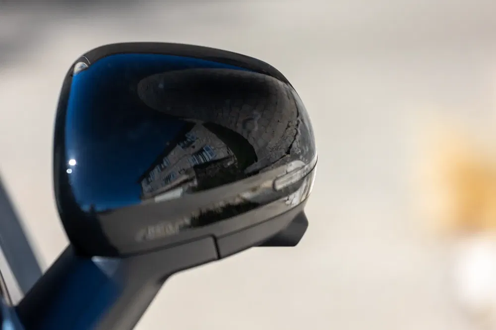 Rétroviseur noir brillant reflétant l'architecture urbaine environnante, focalisé sur ses détails élégants.