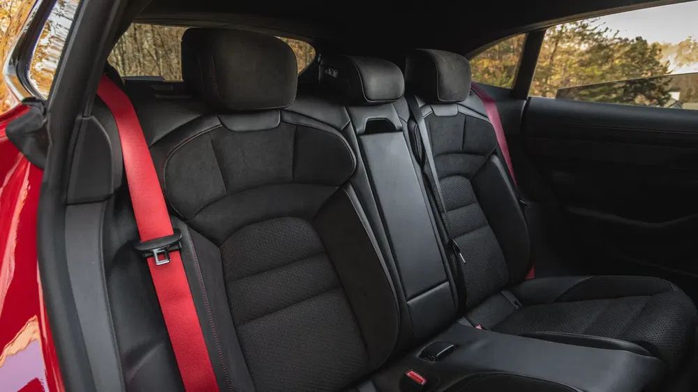 Intérieur de voiture avec sièges arrière en cuir noir et ceintures de sécurité rouges.
