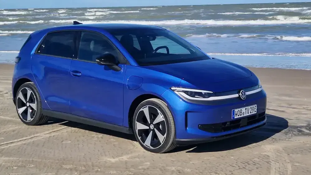 Volkswagen ID.2 tout électrique, bleu, garé sur une plage avec les vagues en arrière-plan.