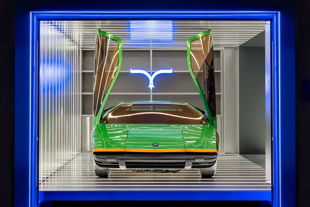 Concept car vert avec portes papillon et logo lumineux en arrière-plan.