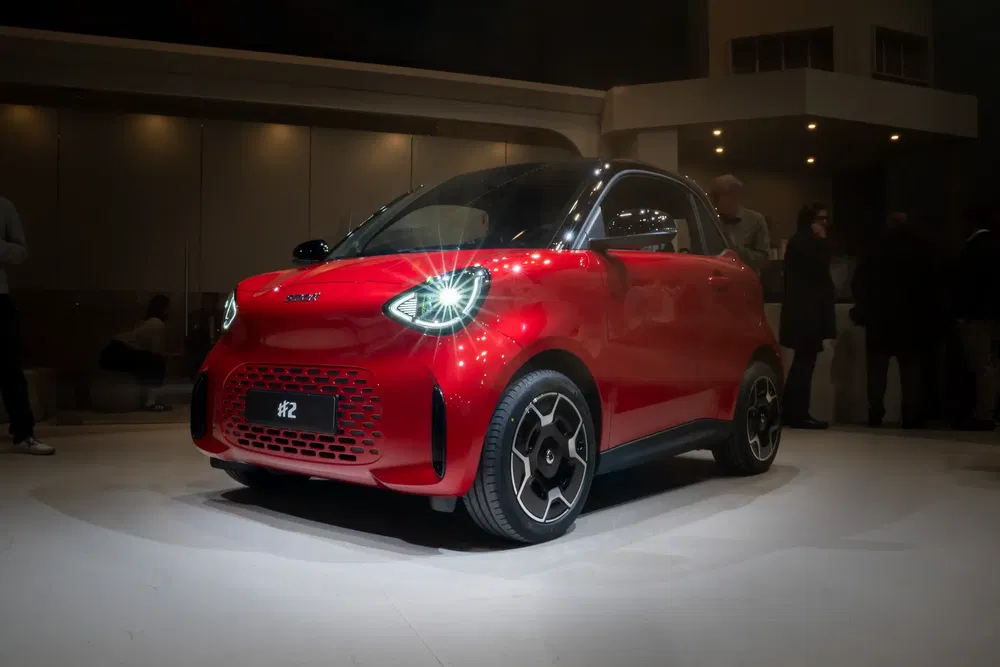Microcar rouge sous des projecteurs, design moderne et compact, lors d'une présentation nocturne.