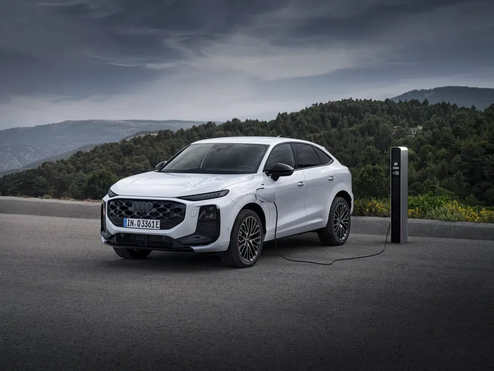 SUV Audi blanc électrique en charge, stationnement en plein air sur fond de forêt.