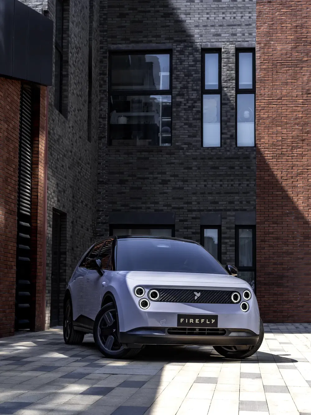 Voiture électrique Firefly moderne garée devant un bâtiment en briques industrielles.