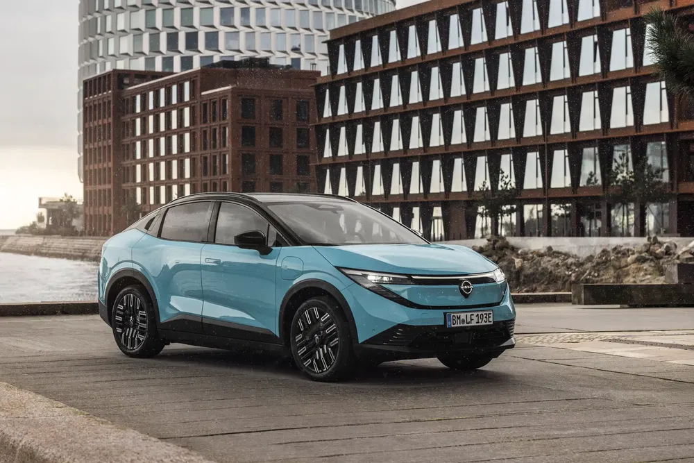 Blauwe elektrische Opel Mokka voor moderne gebouwen aan het water.
