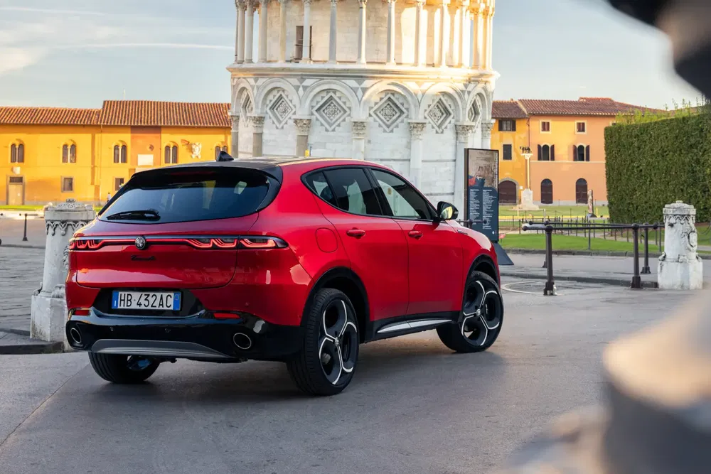 SUV Alfa Romeo rouge devant la Tour de Pise, journée ensoleillée.