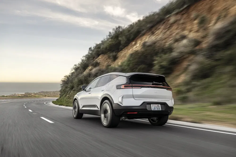 SUV blanc électrique sur route sinueuse bordée de montagne sous un ciel dégagé.