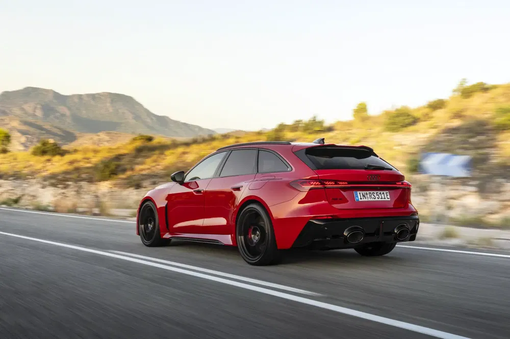 Rode Audi RS-model op zonnige plattelandsweg met bergachtige achtergrond.