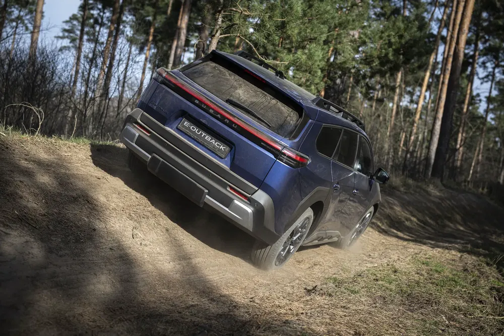 Subaru E-Outback bleu sur terrain boueux en forêt, parfait pour aventures tout-terrain.