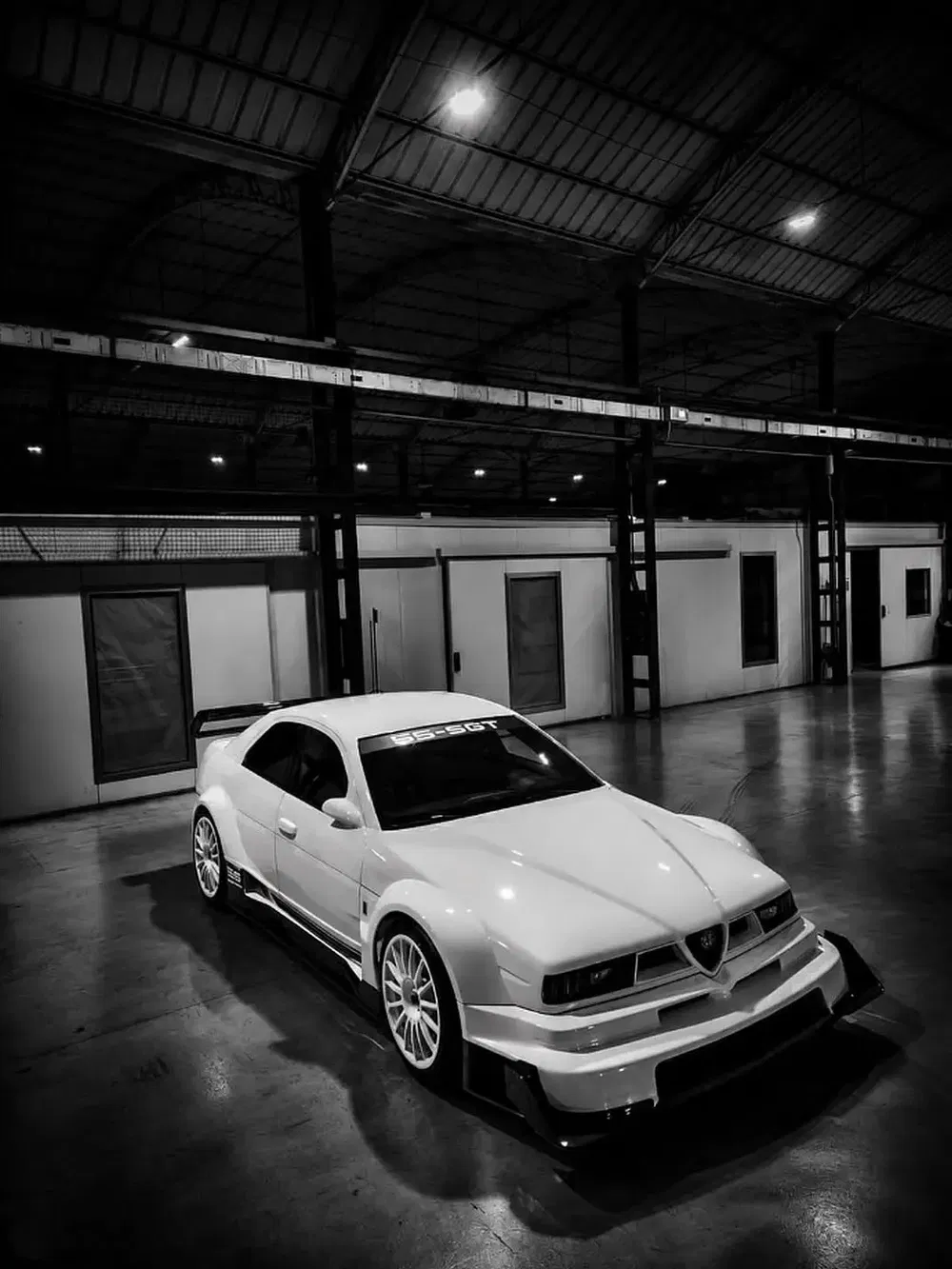 Alfa Romeo SS-GT blanche dans un garage industriel, éclairage minimaliste et contraste élevé.