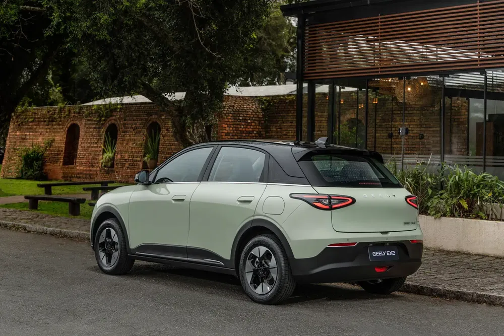 SUV Geely EX3 vert garé près d'un mur de briques et d'un bâtiment moderne.