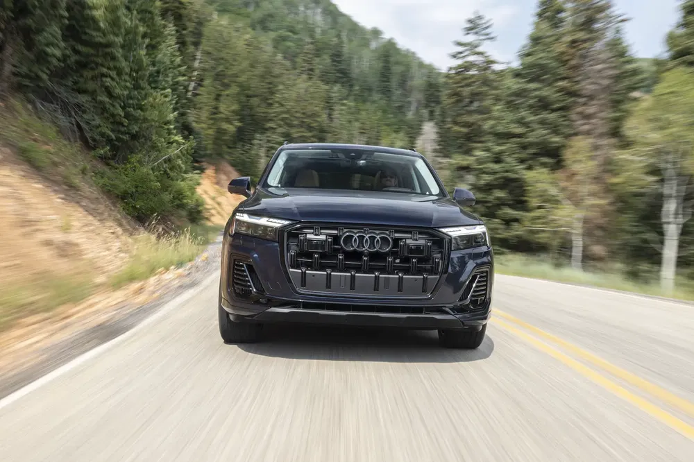 Audi Q7 noire roulant sur une route sinueuse bordée de forêts verdoyantes.