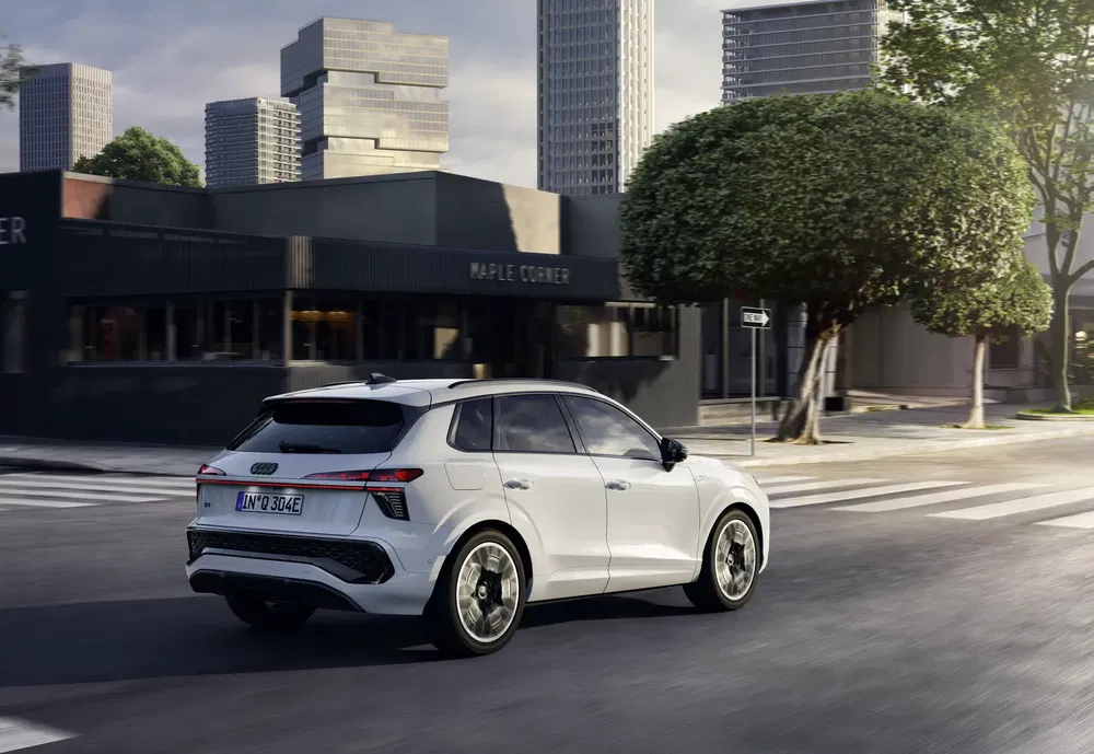Audi Q6 e-tron blanc roulant en ville avec immeubles modernes en arrière-plan.