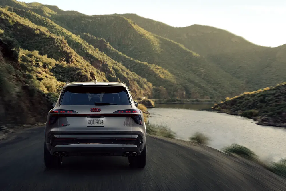 Audi SUV en route de montagne avec lac et collines verdoyantes à l'arrière-plan.