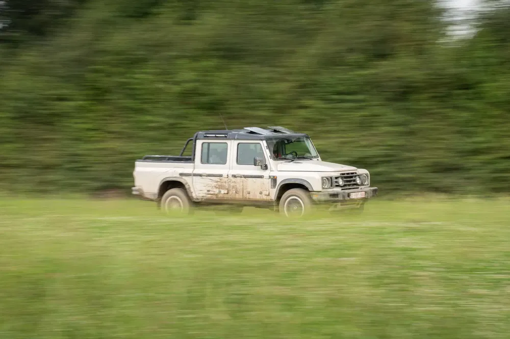 Elektrische Ineos Grenadier 4x4 rijdt over gras, modderige carrosserie.