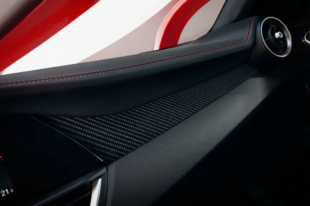 Intérieur de voiture avec détail de garniture en carbone et coutures rouges sportives.