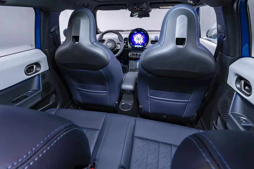 Intérieur d'une Mini Cooper moderne avec sièges avant, tableau de bord numérique et écran rond distinctif.
