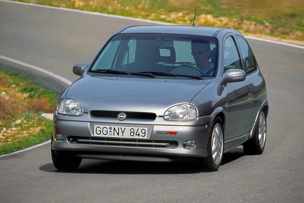 Opel Corsa B GSi argentée en virage sur route sinueuse.